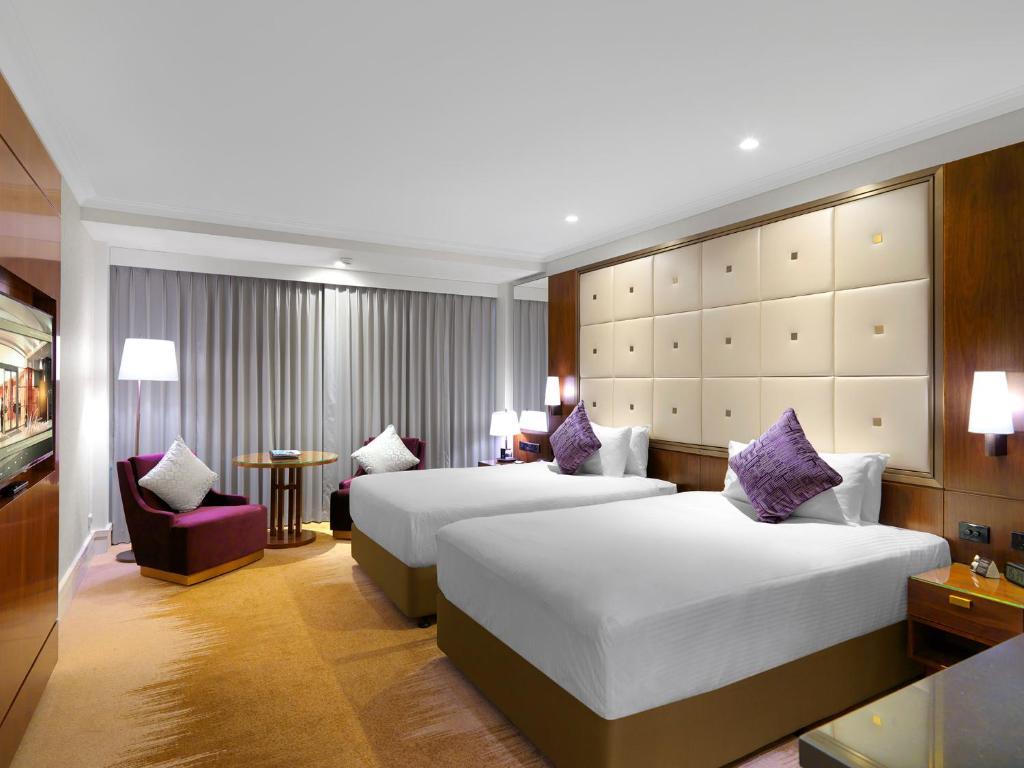 Amora Hotel Jamison Сідней Екстер'єр фото The photo shows a modern hotel room featuring two beds with white sheets and purple accent pillows. There is a stylish headboard behind the beds, and the room is well-lit with lamps on bedside tables. A seating area includes a purple chair and a smal