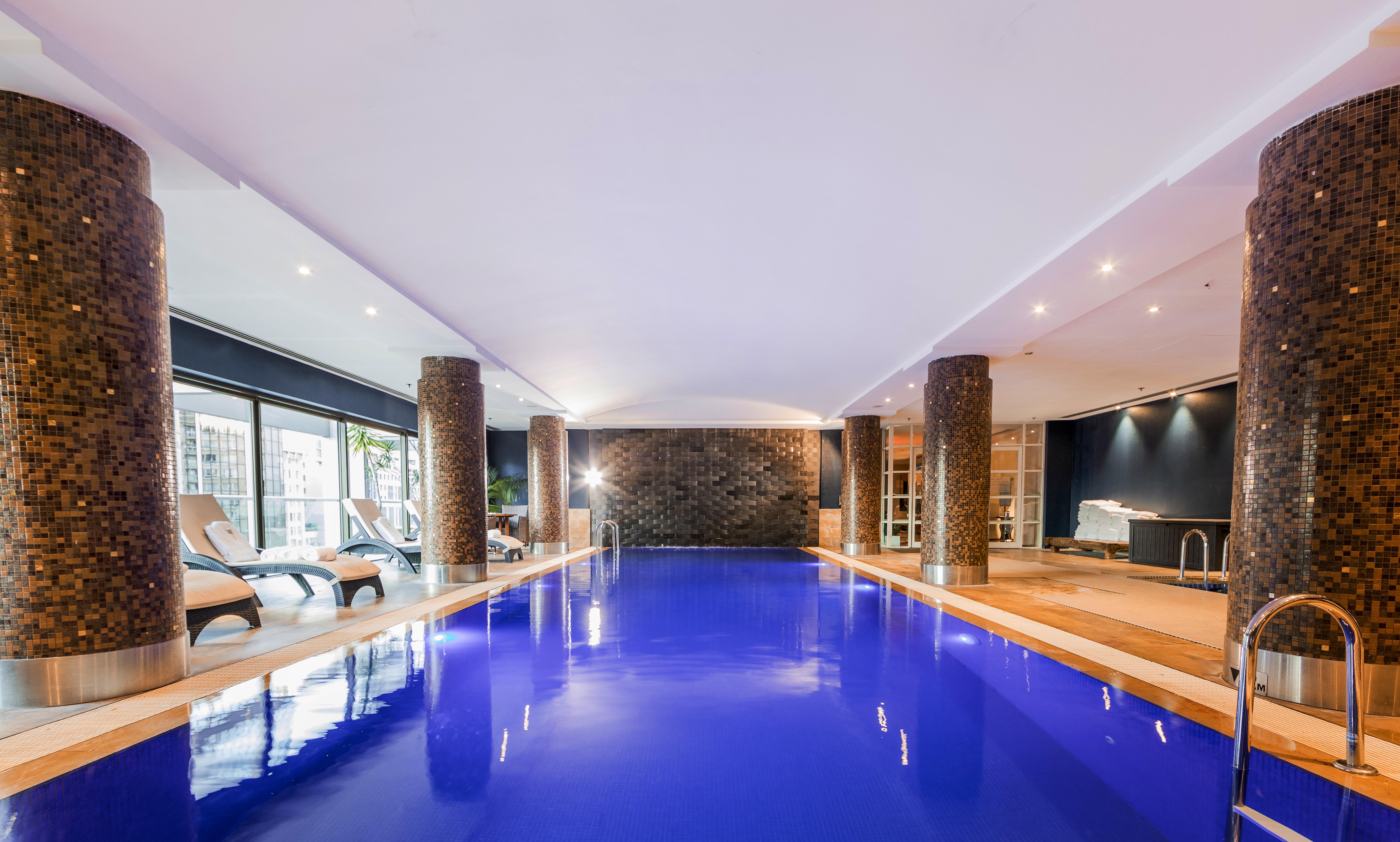 Amora Hotel Jamison Сідней Екстер'єр фото The photo shows an indoor swimming pool. The water is a striking blue color, and the surrounding area has modern decor. There are stone columns supporting the ceiling, and the lighting is bright and inviting. To one side, there are several lounge cha