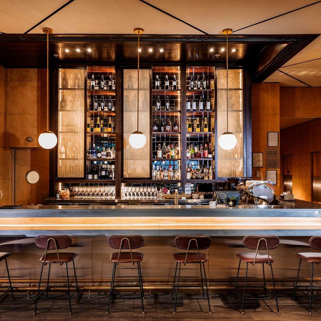 Amora Hotel Jamison Сідней Ресторан фото The photo shows a well-designed bar area. The bar has an elegant, modern aesthetic with a long, polished countertop and several backlit pendant lights hanging above. Behind the bar, there are shelves filled with various bottles of liquor, displayed n