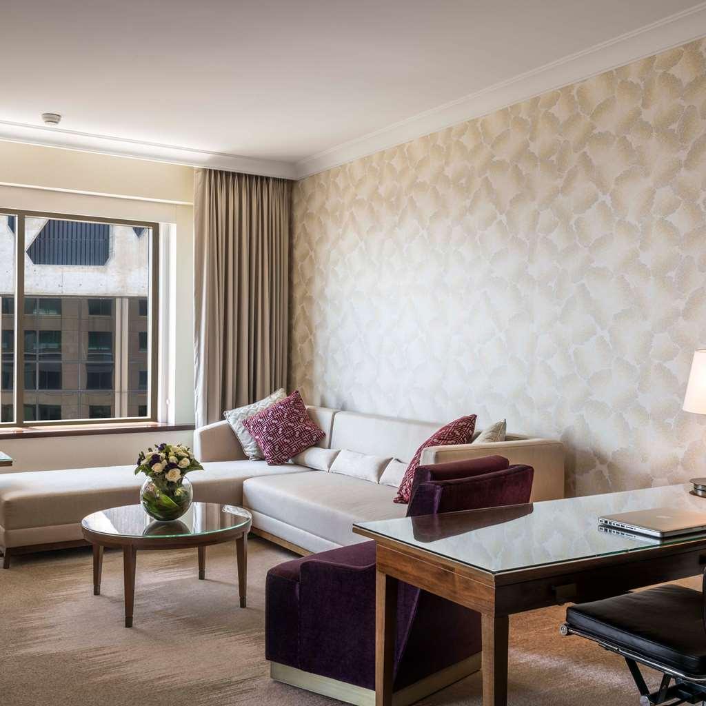 Amora Hotel Jamison Сідней Номер фото The photo depicts a modern and stylish living area. It features a light-colored sofa with decorative cushions, a coffee table in the center, and a desk with a chair. The walls are adorned with a patterned wallpaper, and there are large windows lettin