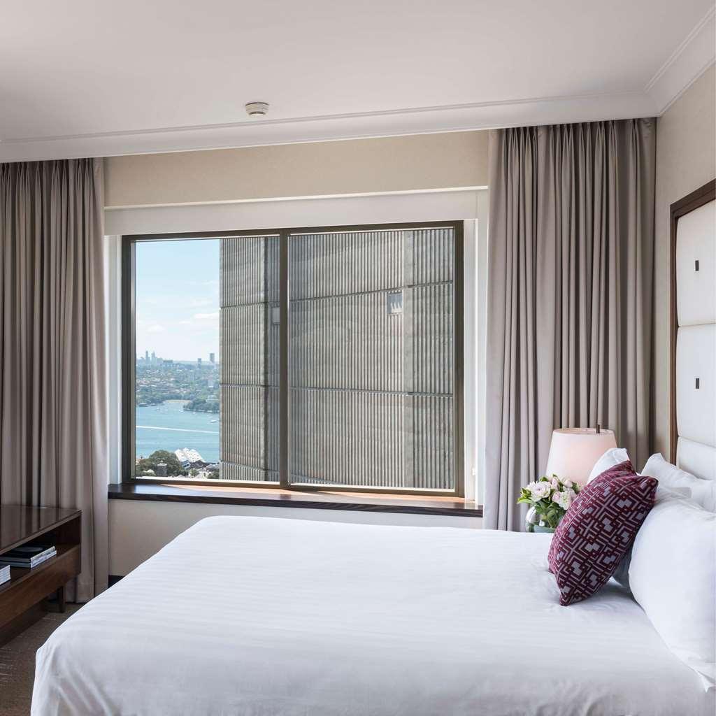 Amora Hotel Jamison Сідней Номер фото The photo shows a modern hotel room with a large window that offers a view of the outside. The room features a neatly made bed with white bedding and a decorative pillow. There are light-colored curtains framing the window, which appears to overlook 