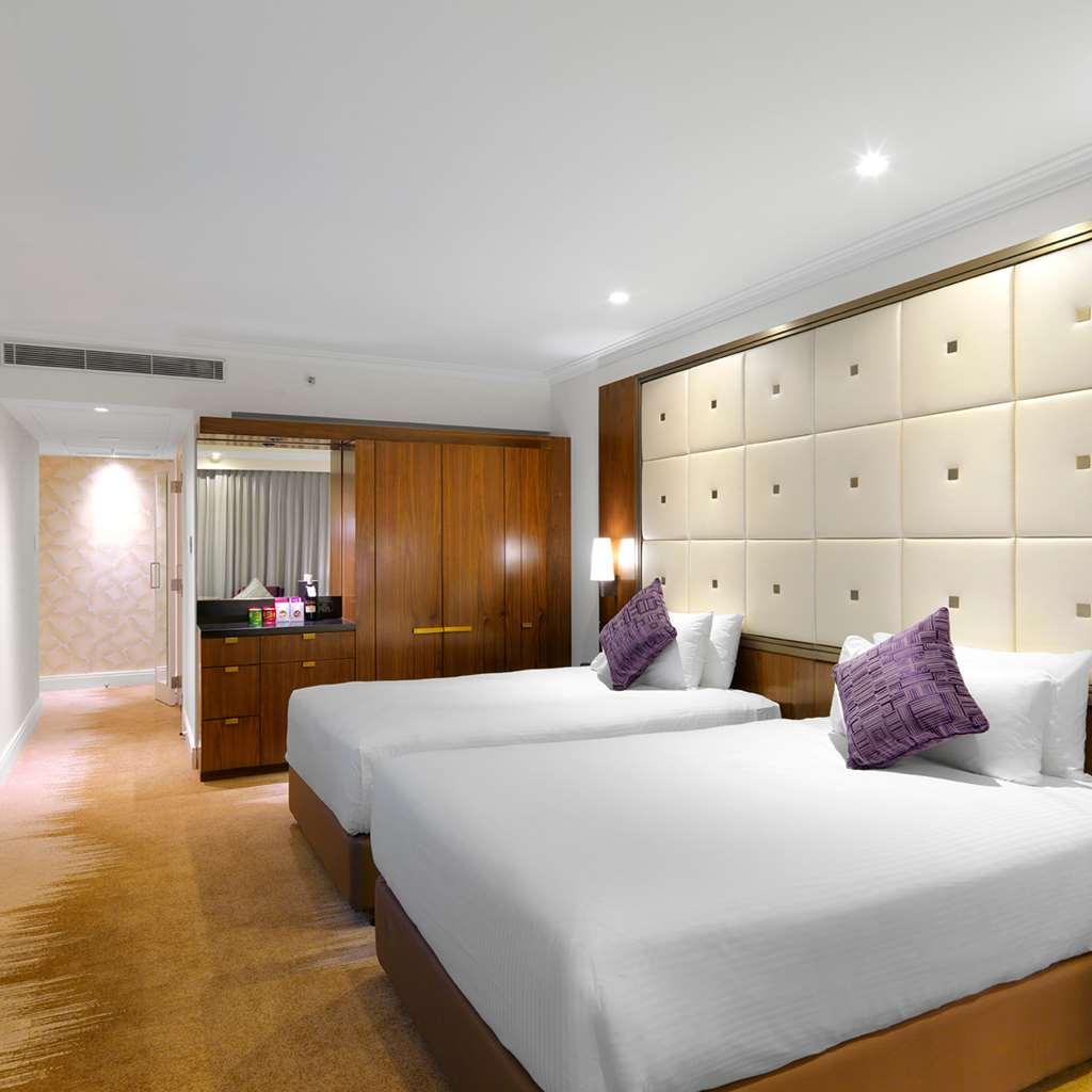 Amora Hotel Jamison Сідней Номер фото The photo shows a modern hotel room featuring two twin beds with white bedding and purple decorative pillows. The walls are designed with soft beige panels, creating a luxurious ambiance. There’s wooden furniture, including a cabinet against one wall
