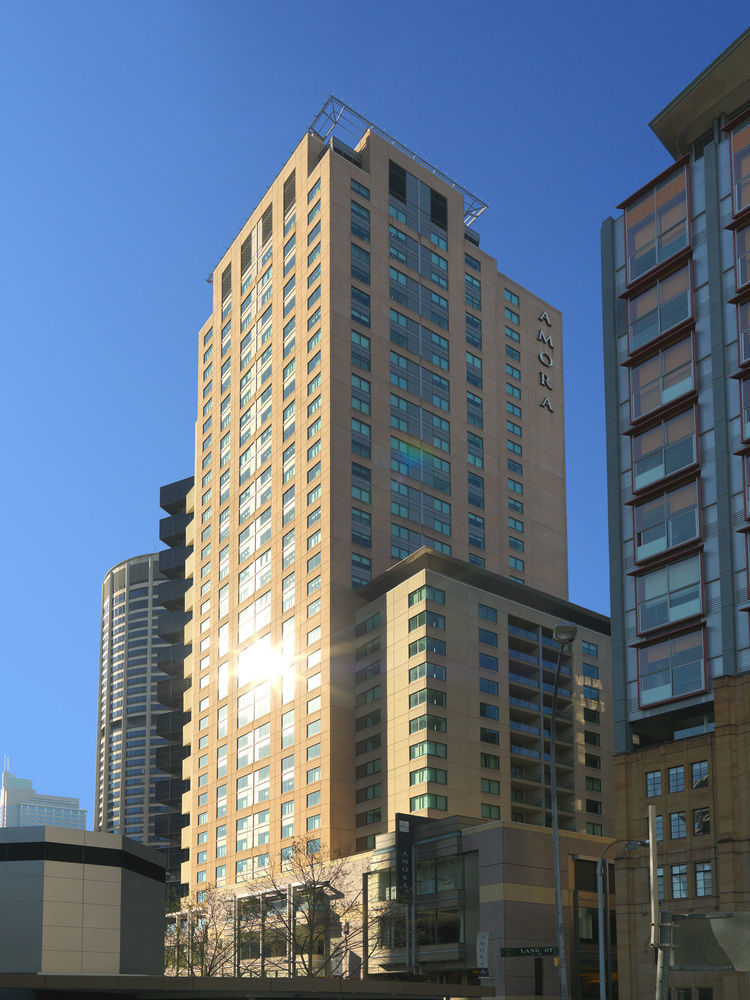 Amora Hotel Jamison Сідней Екстер'єр фото The photo shows a tall building with a modern architectural design, featuring a mix of glass and concrete materials. The building is predominantly light-colored with large windows reflecting sunlight. It appears to have multiple floors, and the name 