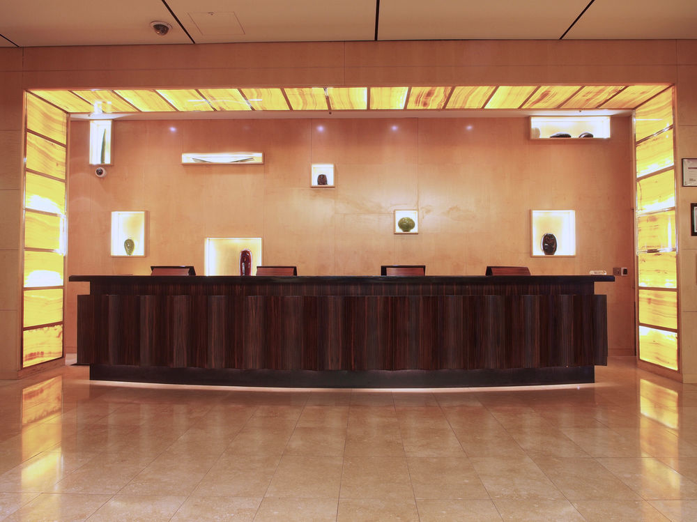 Amora Hotel Jamison Сідней Екстер'єр фото The photo shows a modern reception area. At the center is a sleek, dark wood reception desk. Behind the desk, there is a wall that features illuminated sections in warm tones, creating an inviting atmosphere. There are several small display niches in
