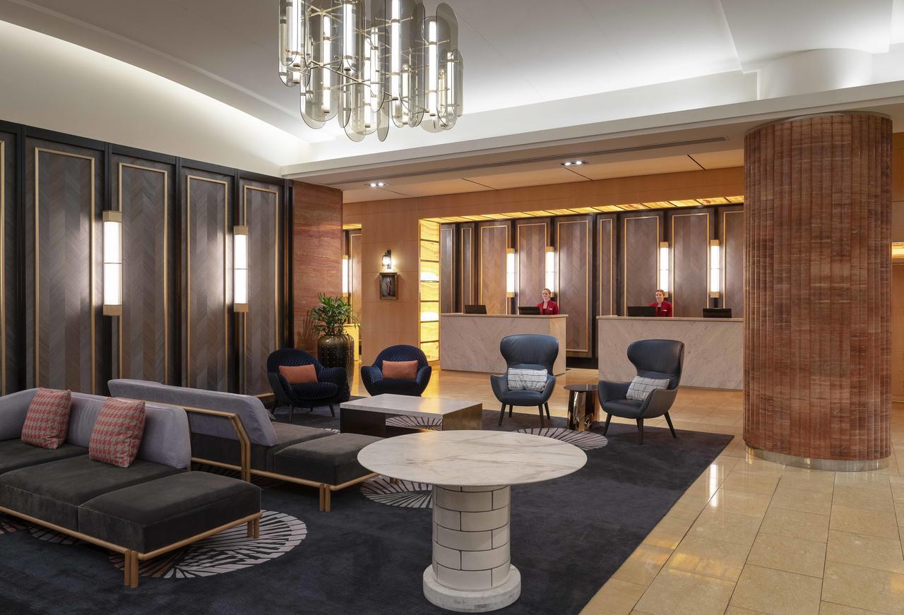 Amora Hotel Jamison Сідней Екстер'єр фото The photo depicts a modern hotel lobby. It features stylish furniture, including a black and gray seating area with cushions, and two blue accent chairs. A round, white coffee table sits in the center of the seating arrangement. The background shows 