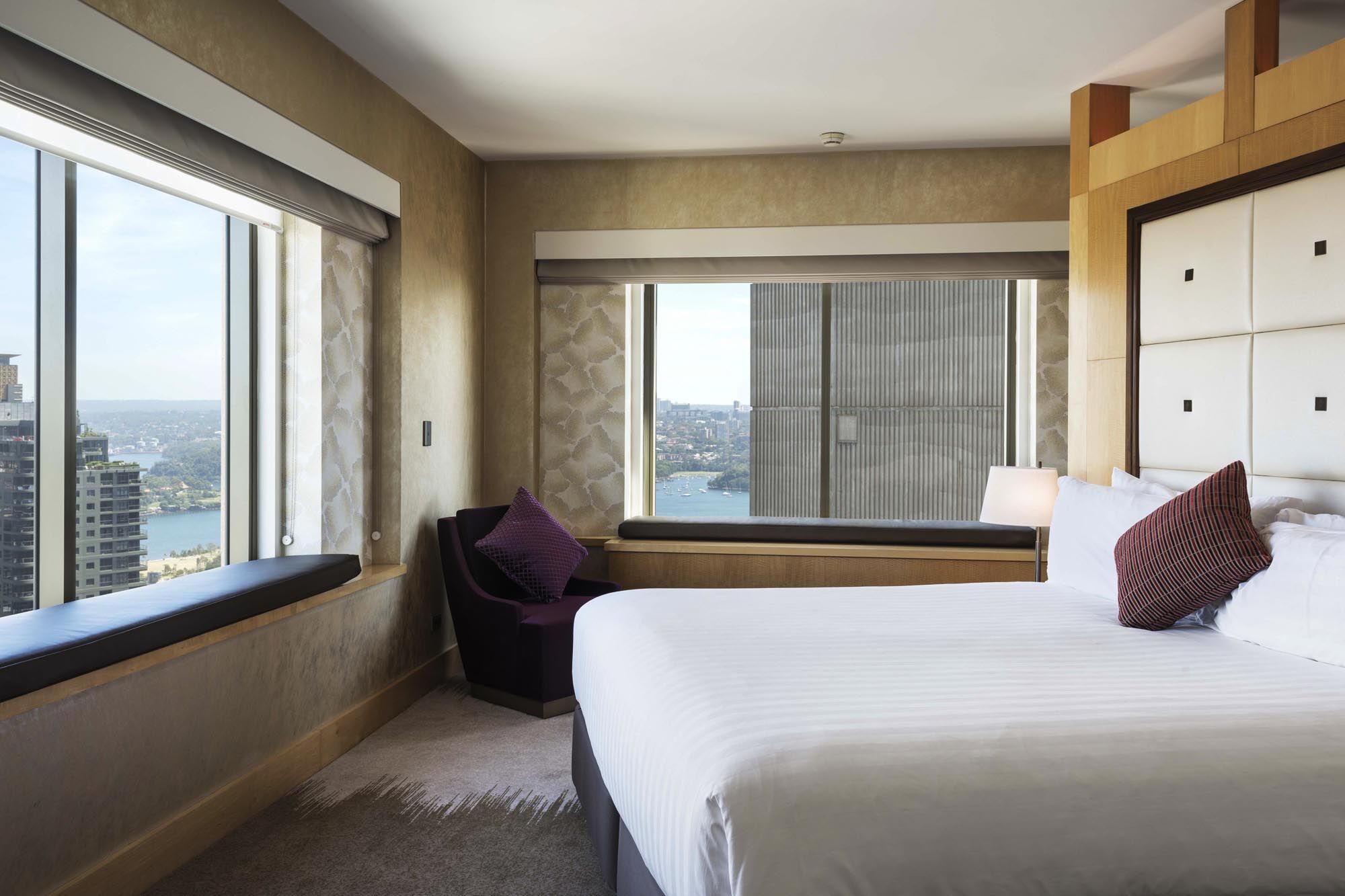 Amora Hotel Jamison Сідней Екстер'єр фото The photo shows a modern, stylish hotel room featuring a bed with white linens, a decorative pillow, and a cozy chair with a purple cushion. Large windows provide a view of the outside scenery, which appears to include a body of water and buildings. 