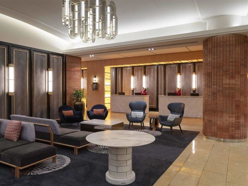 Amora Hotel Jamison Сідней Екстер'єр фото The photo depicts a stylish hotel lobby. There are several modern seating arrangements featuring dark upholstered couches and armchairs placed around a round marble coffee table. The design incorporates a combination of elegant lighting fixtures and 