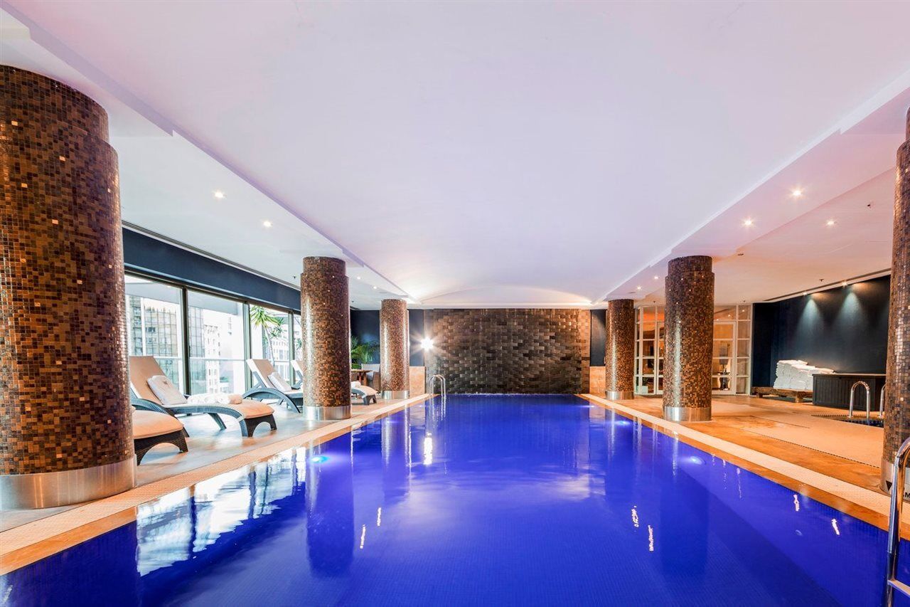 Amora Hotel Jamison Сідней Екстер'єр фото The photo features an indoor swimming pool with vibrant blue water. The pool area is well-lit, with several sources of light illuminating the space. Surrounding the pool are stylish stone columns, and there are lounge chairs positioned nearby for rel